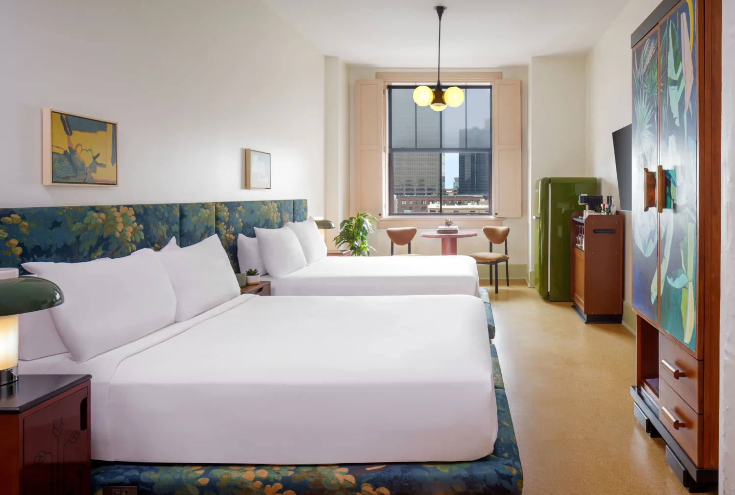 Boutique hotel room featuring two beds, stylish lamps, and a window view of the New Orleans city skyline