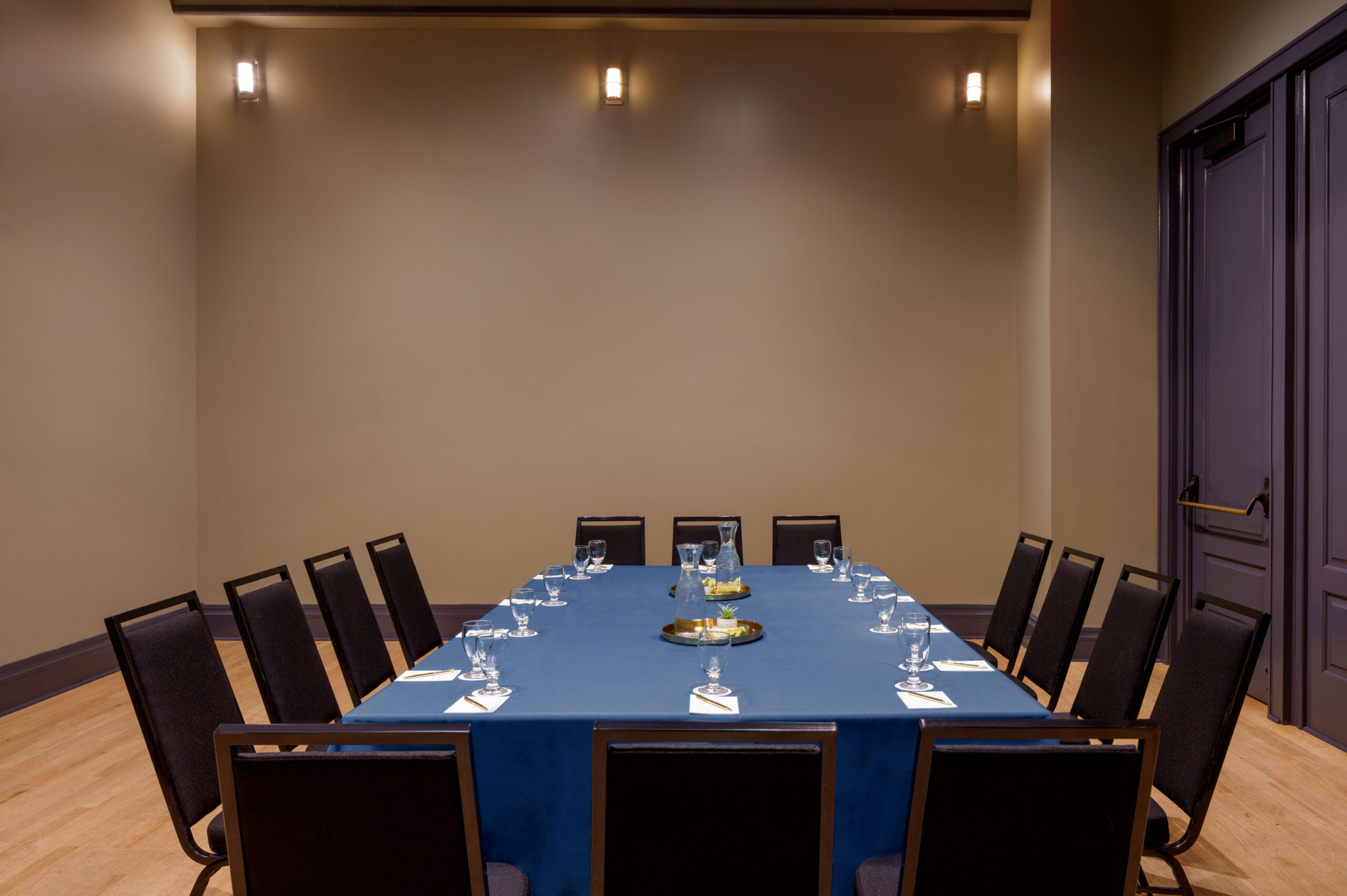 Brightly lit meeting room featuring a long table set with water pitchers and dark padded chairs