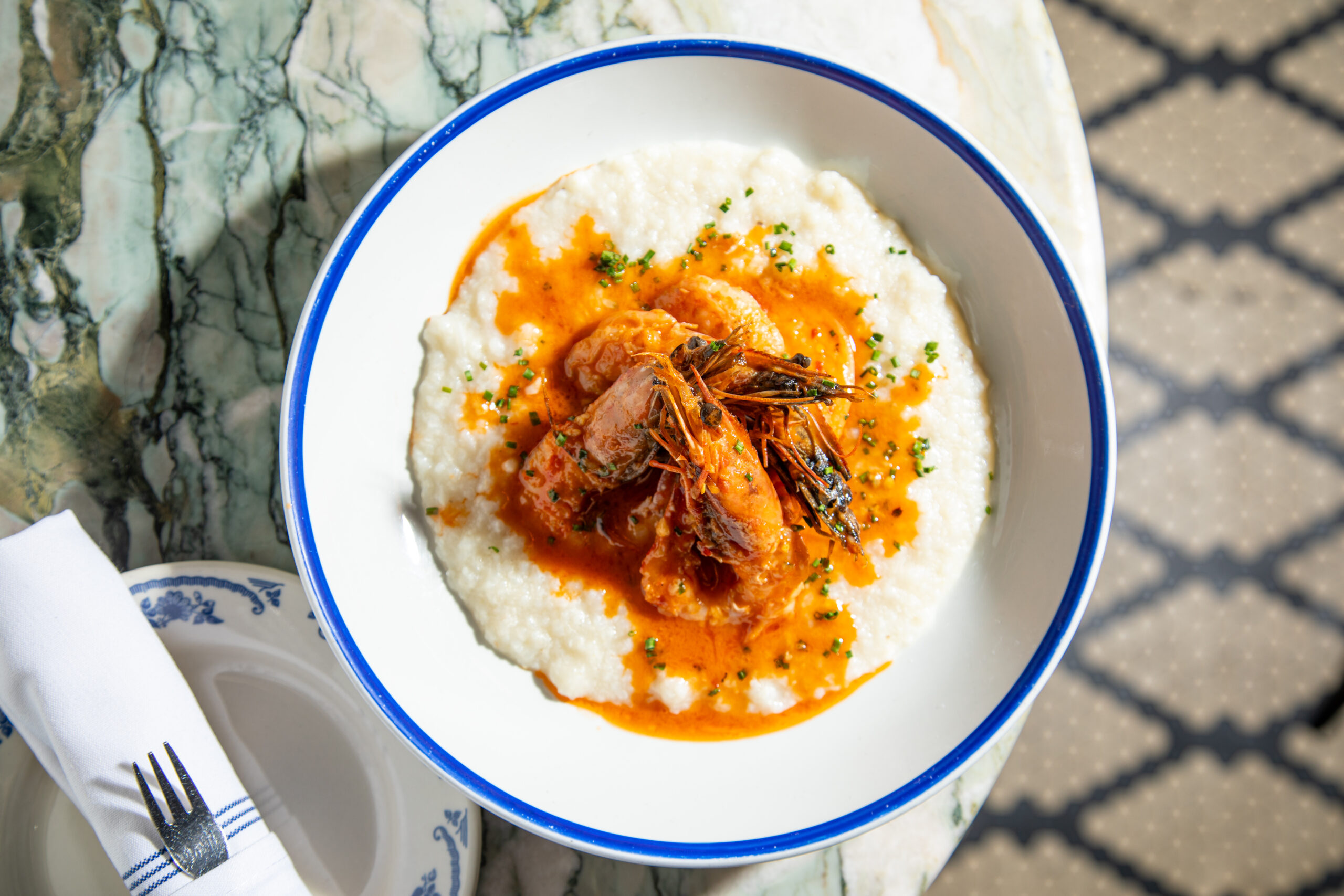 Overhead view of traditional New Orleans shrimp and grits with rich orange sauce on a marble table