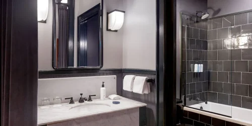 Elegant hotel bathroom featuring a marble sink, vintage black fixtures, and a shower with dark tiled walls