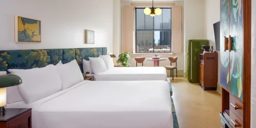 Boutique hotel room featuring two beds, stylish lamps, and a window view of the New Orleans city skyline