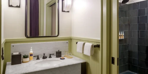 Elegant hotel bathroom featuring a marble sink, vintage black fixtures, and a shower with dark tiled walls