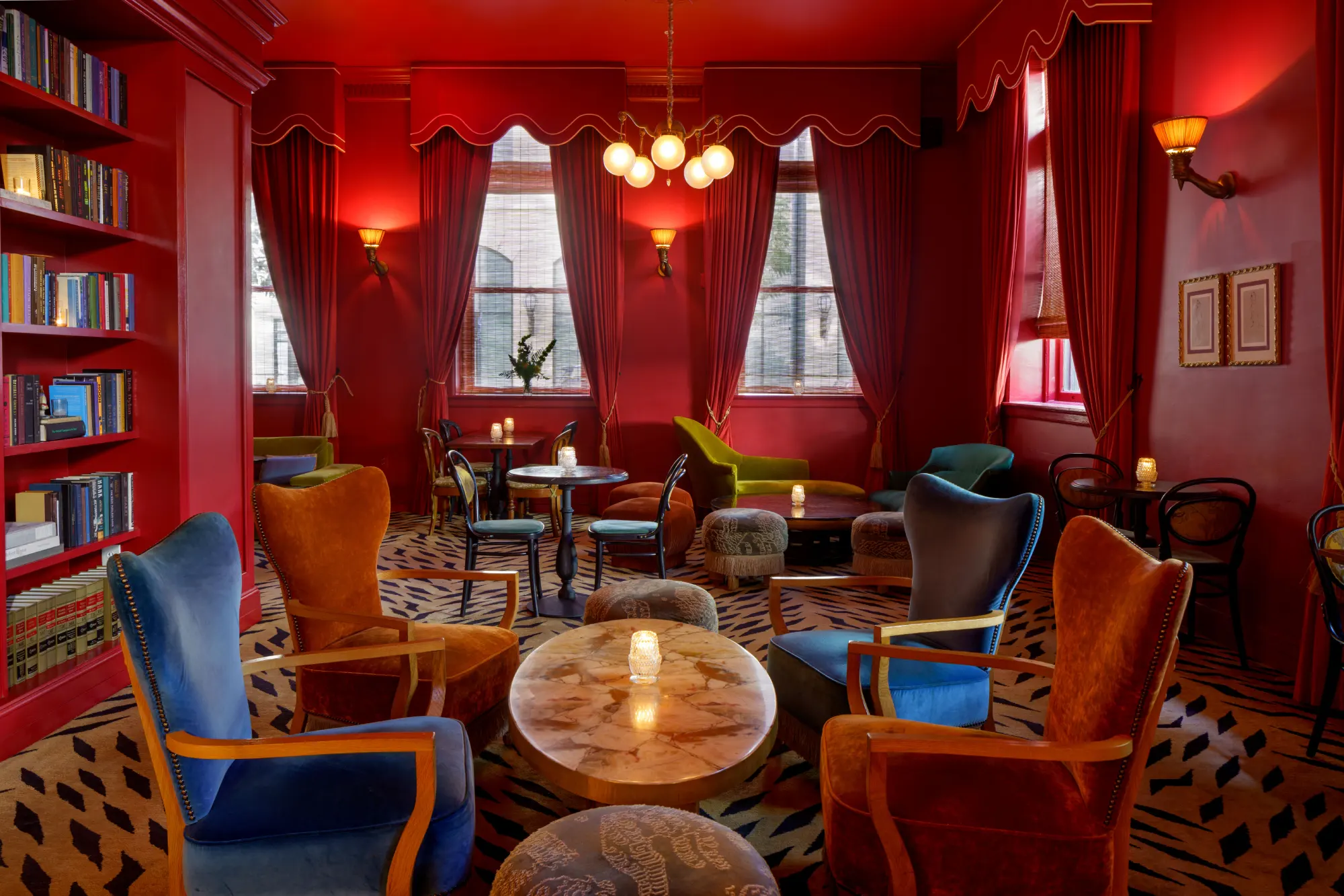 Professional shot of the dramatic red hotel library lounge with velvet chairs and candlelit tables