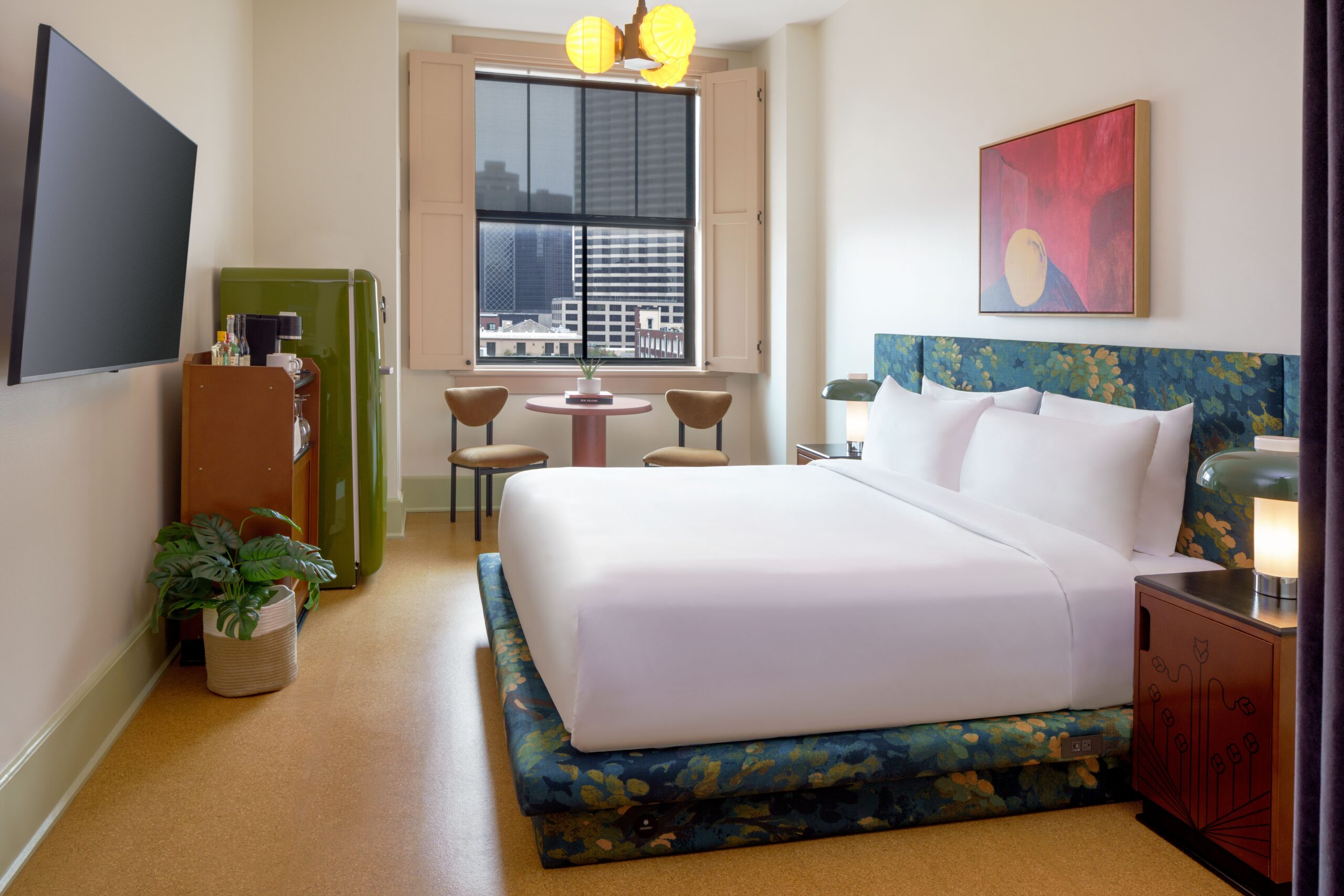 Professional shot of a stylish hotel suite with a patterned bed, retro fridge, and downtown view