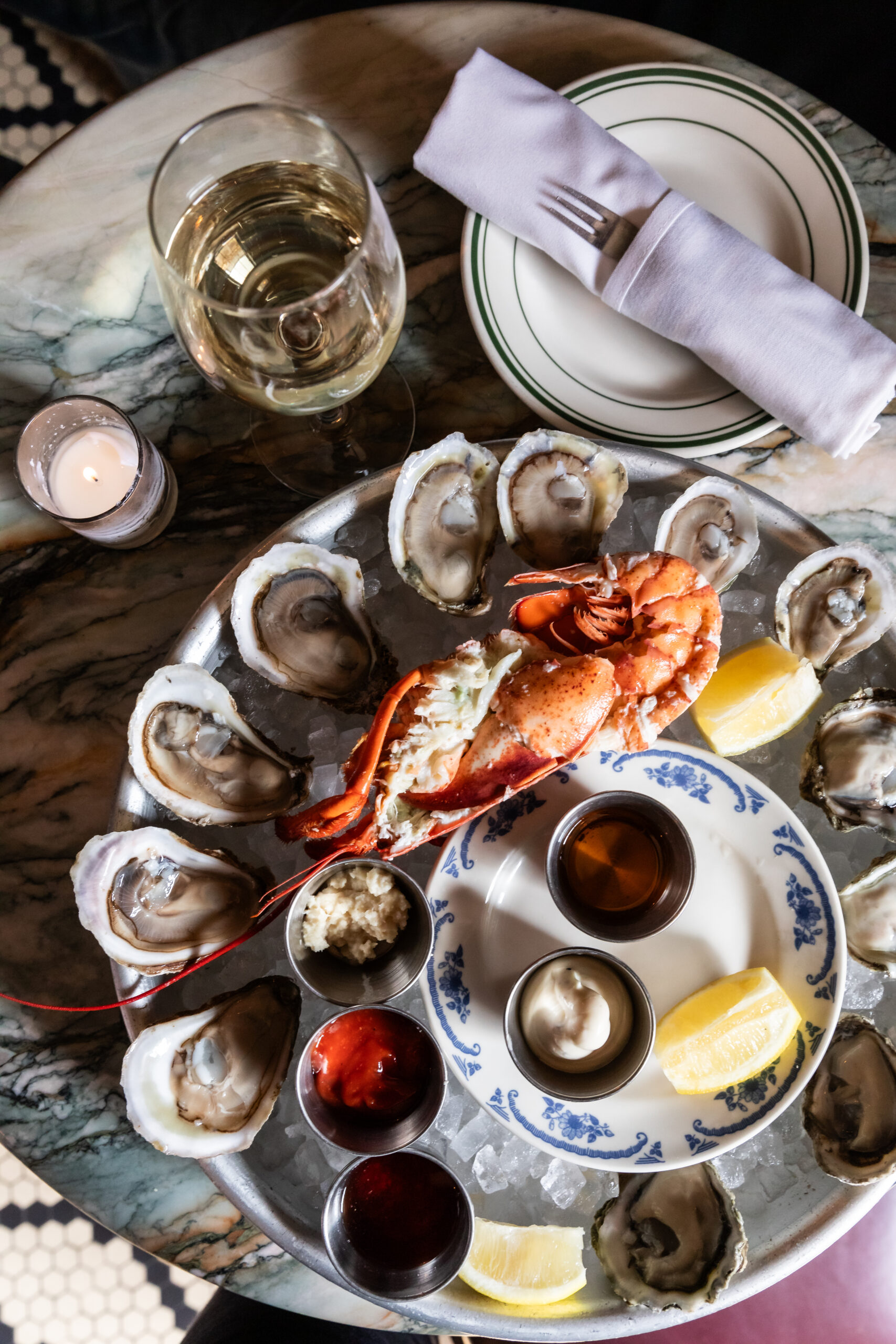 Detailed close-up showing fresh oysters and halved lobster served on ice with wine and cocktail sauces