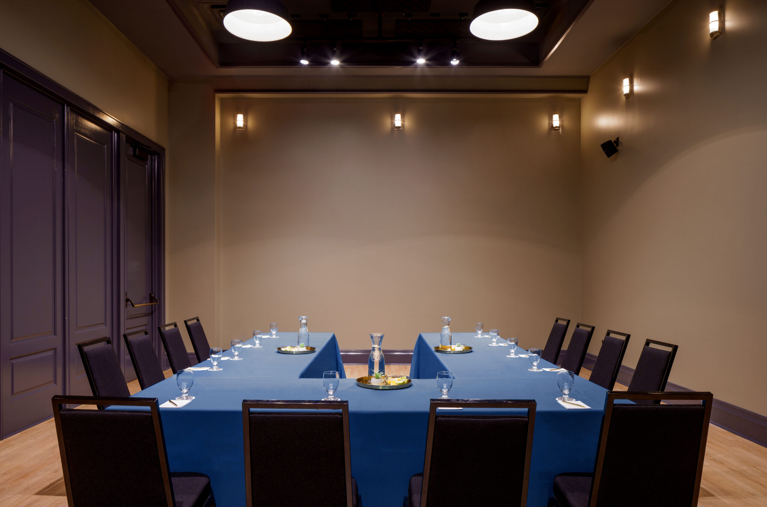 Brightly lit hotel meeting space featuring a U-shaped table set with water glasses and notepad stations