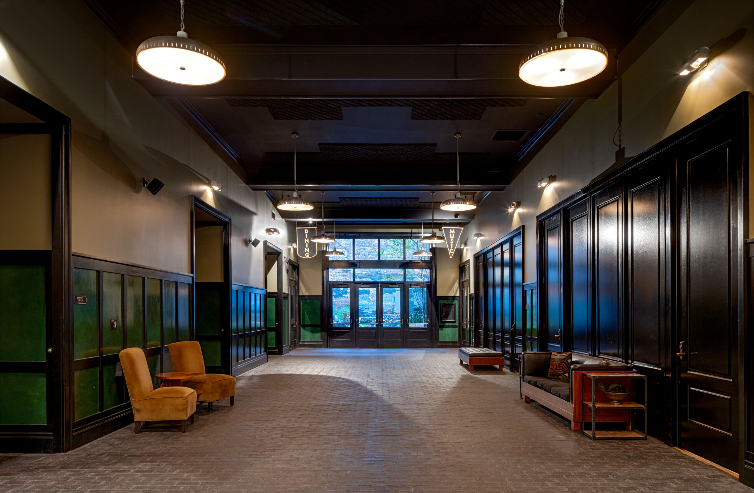 Dramatic view of the dark, long hotel corridor with green paneling and vintage velvet lounge seating