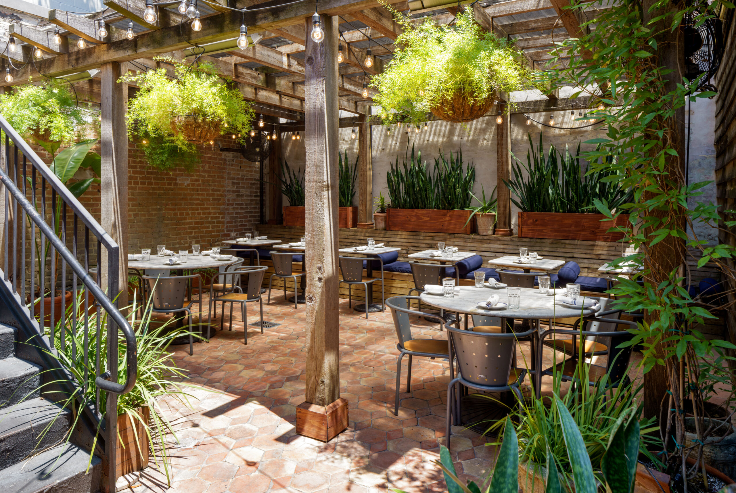 Brightly lit courtyard patio featuring marble tables under a vine-covered pergola, ideal for New Orleans bars