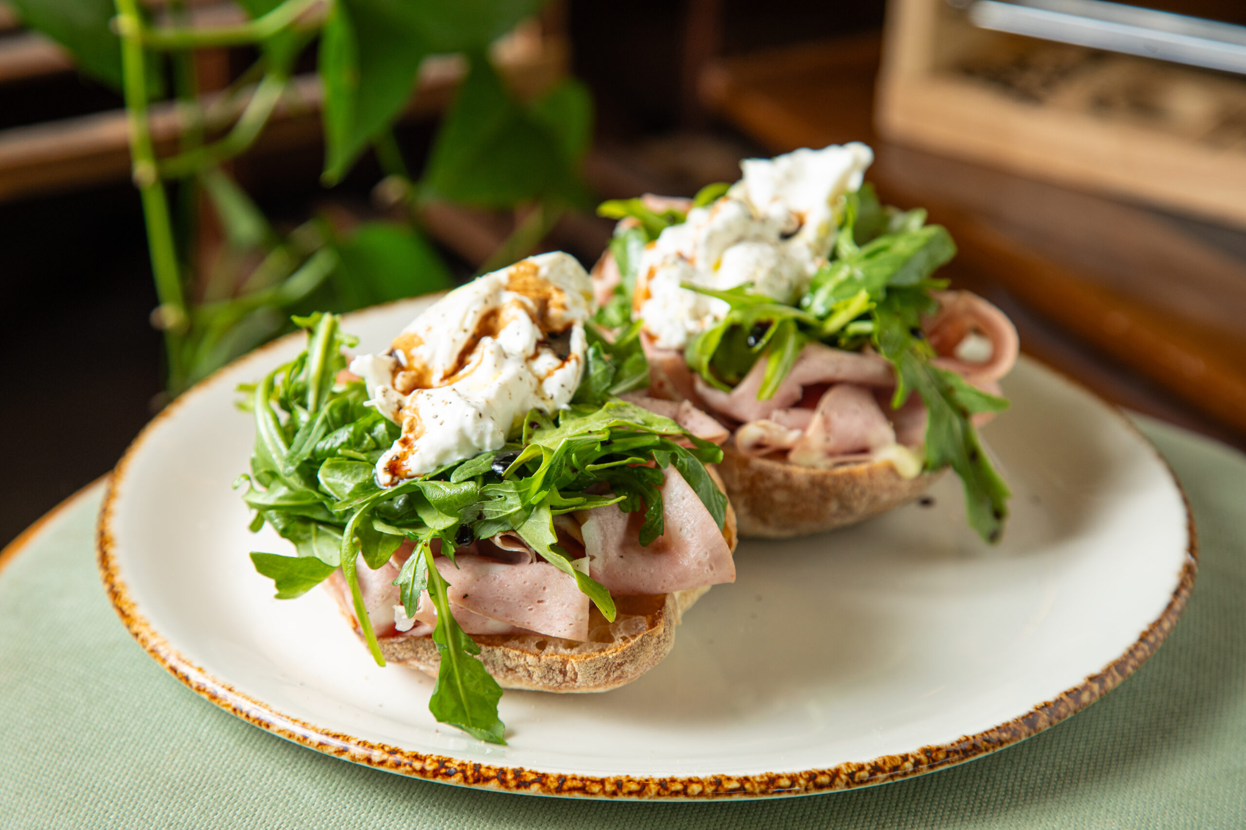 Detailed close-up showing two bruschetta style snacks with sliced meat, arugula, and creamy cheese