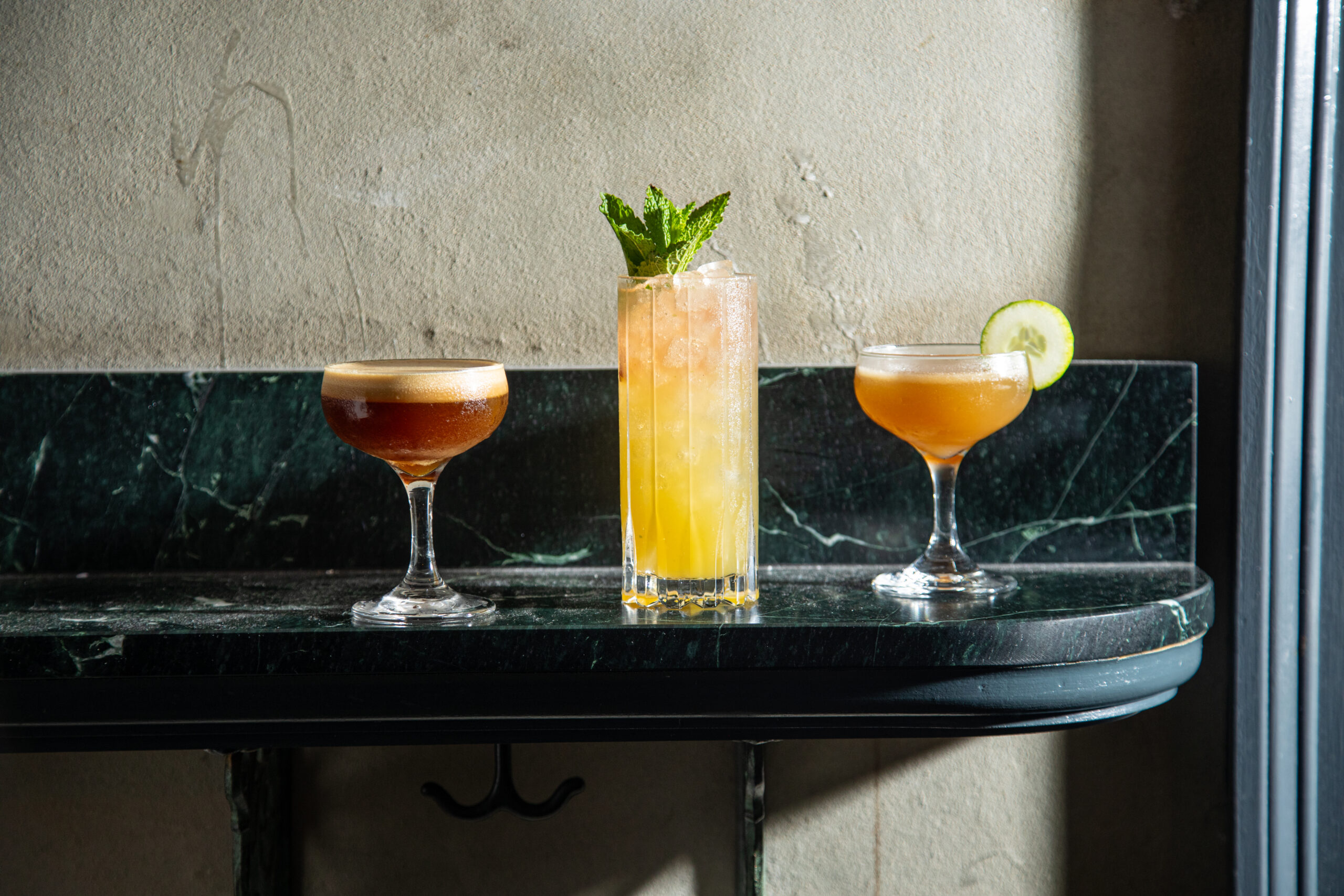 Detailed close-up showing three different cocktails on a dark green marble counter