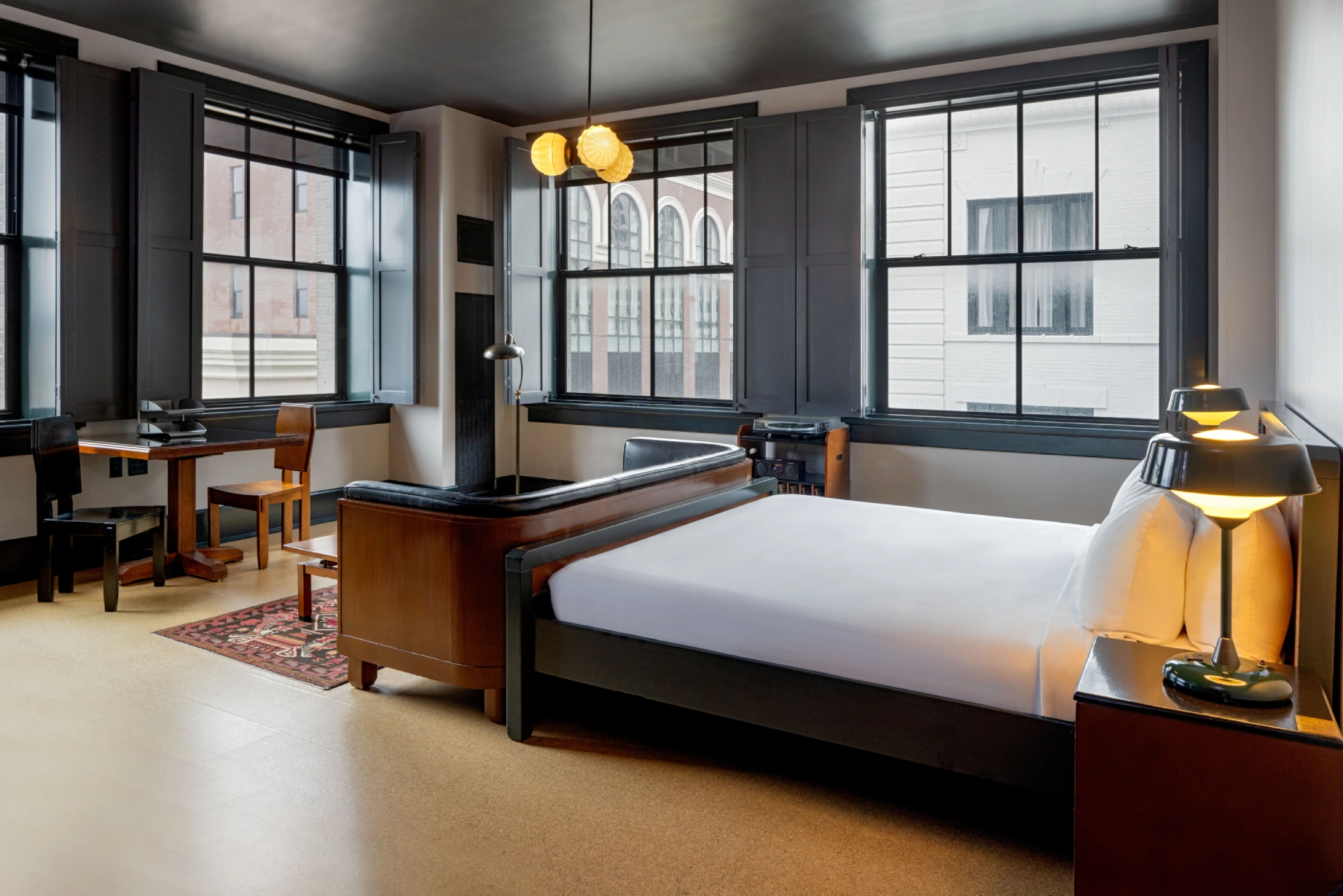 a hotel room with a bed, desk, and two windows