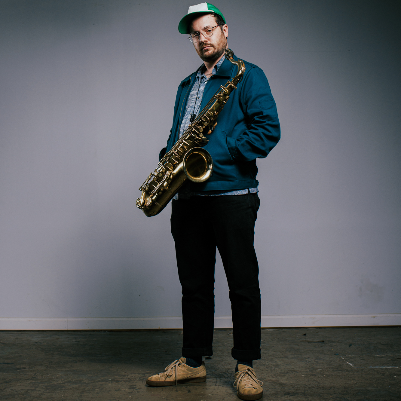 Byron Asher holding a saxophone standing in front of a grey wall.