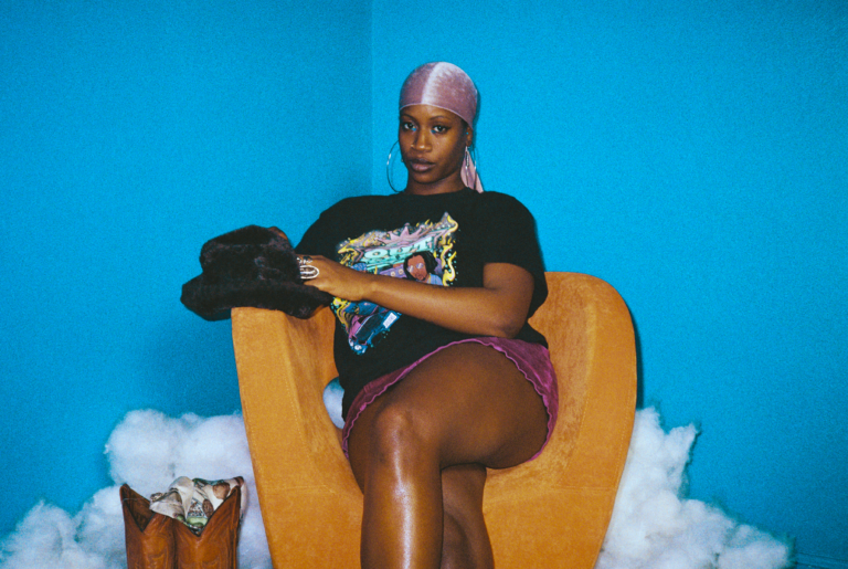 Cristen "Ten" Spencer sitting in a yellow chair in front of a blue wall.